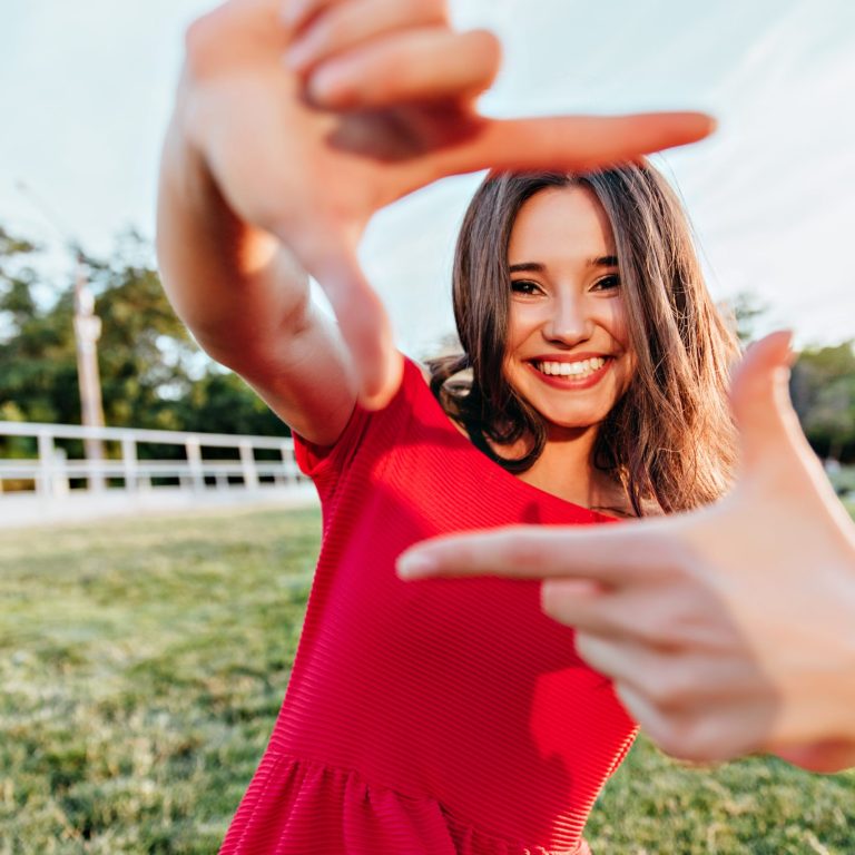 Spectacular brunette girl enjoying summer photoshoot on nature background. Magnificent lady with happy face expression fooling around in park in weekend.